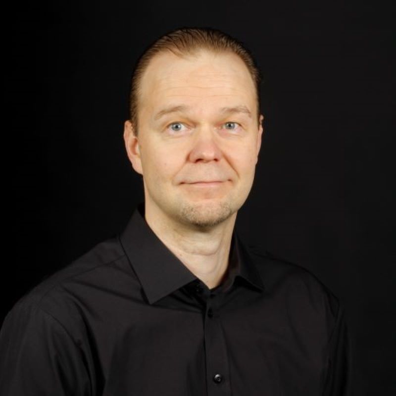 Muotokuva henkilöstä mustassa kauluspaidassa ja tummalla taustalla.