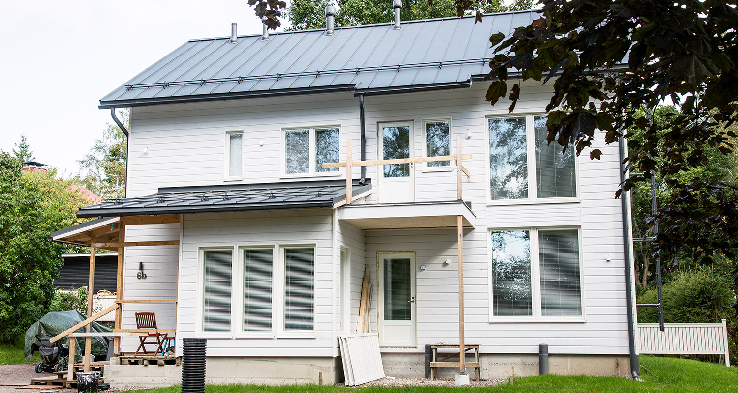 Kaksikerroksinen valkoinen puutalo mustalla peltikatolla, ikkunoita ja rakennustelineitä