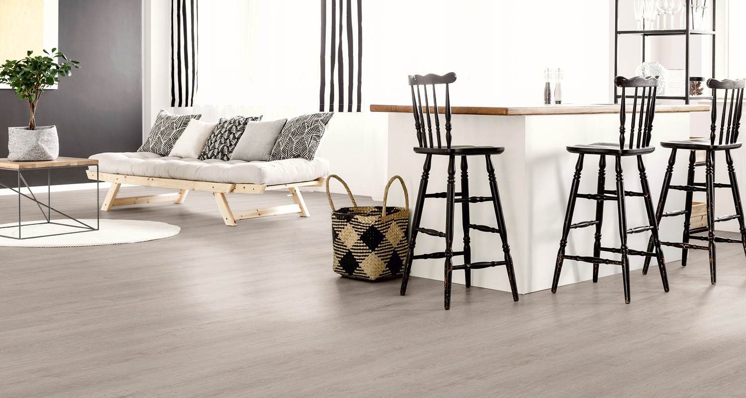 Vaalea olohuone-keittiö: vaalea sohva mustavalkotyynyillä, vaalea puulattia, mustat baarijakkarat