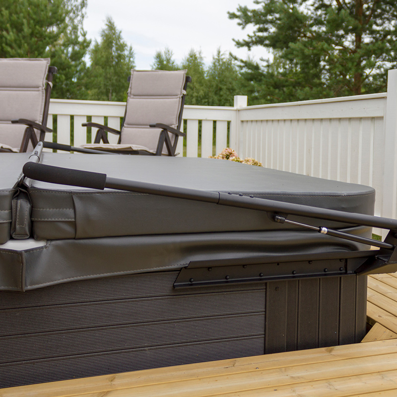 Musta porealtaan kansi nostotangolla terassilla, harmaat tuolit ja valkoinen aita.