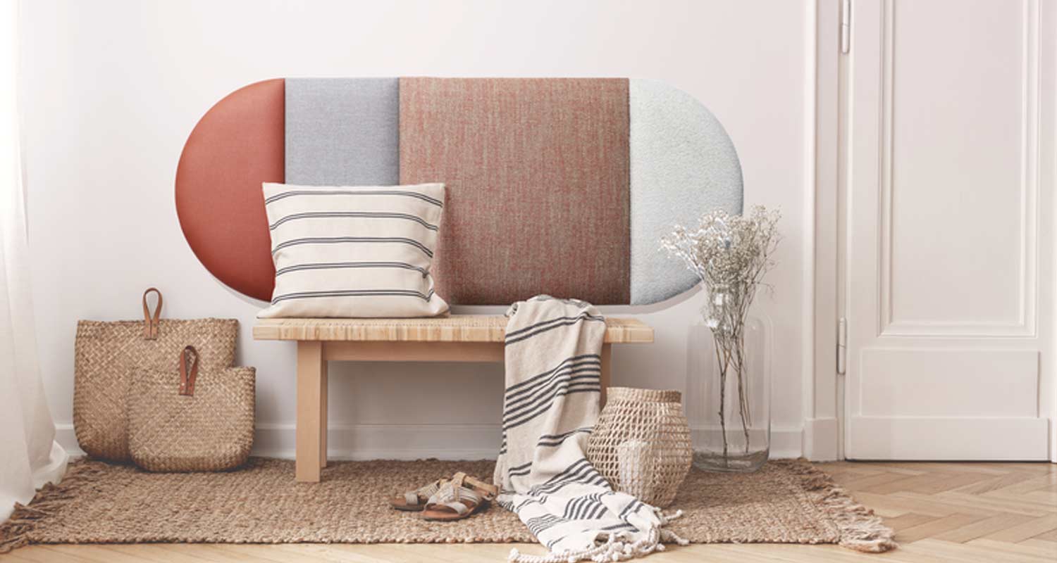 Vaalea eteinen: puupenkki monivärisellä selkänojalla, raidallinen tyyny ja viltti, korikassit.