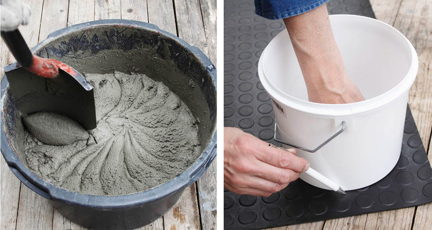 Mustassa ämpärissä harmaata betonia lapio, viereisessä valkoisessa ämpärissä käsi merkitsemässä.