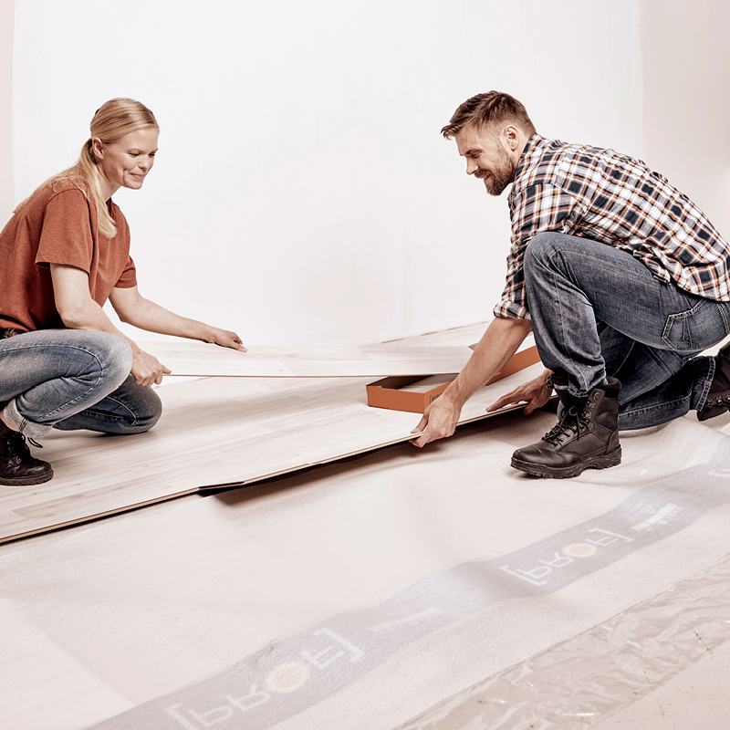 Mies ja nainen polvillaan asentavat vaaleaa laminaattilattiaa valkoisessa huoneessa