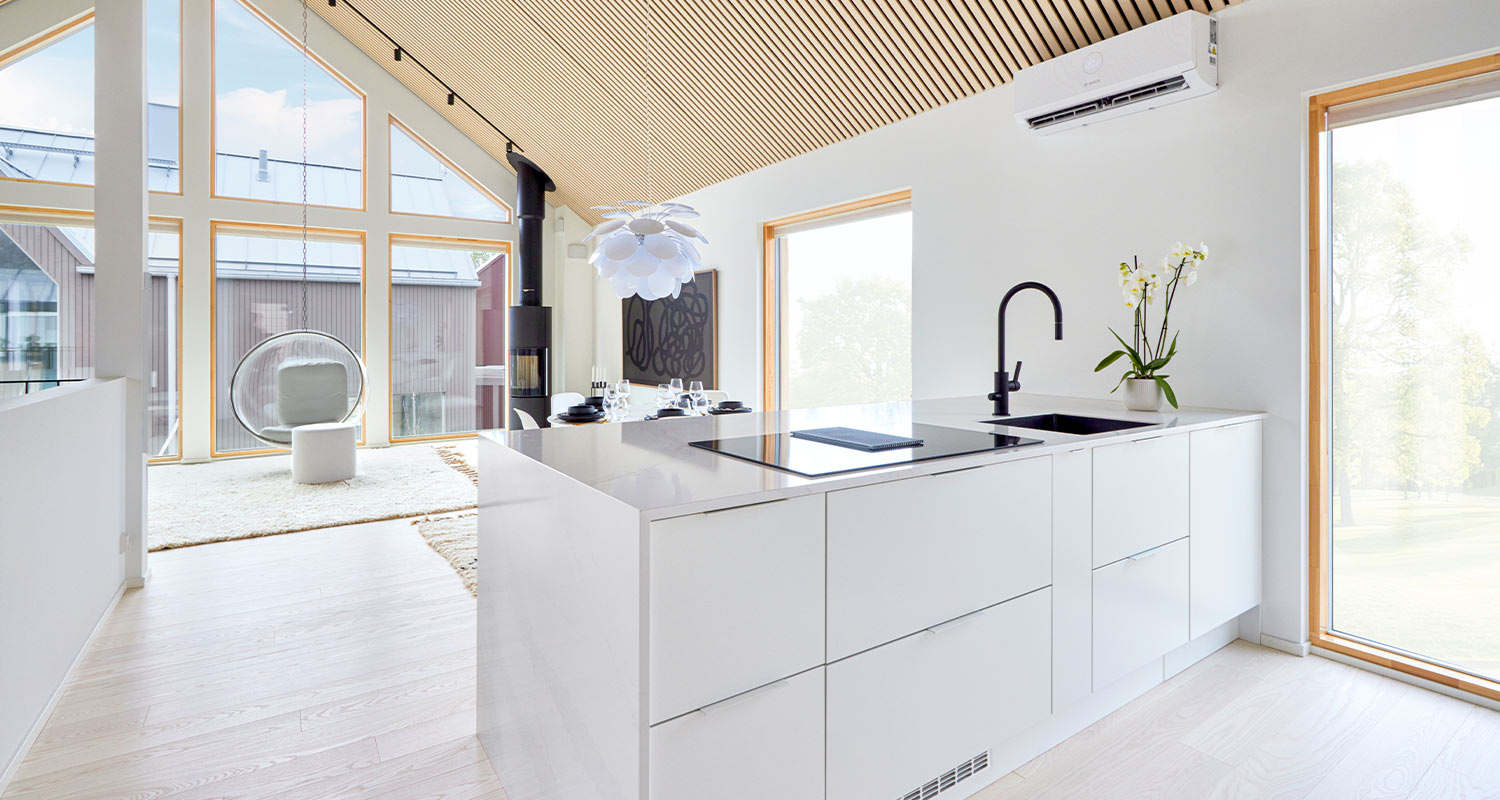 Valoisa avoin keittiö-olohuone valkoisella saarekkeella, musta hana ja suuret ikkunat