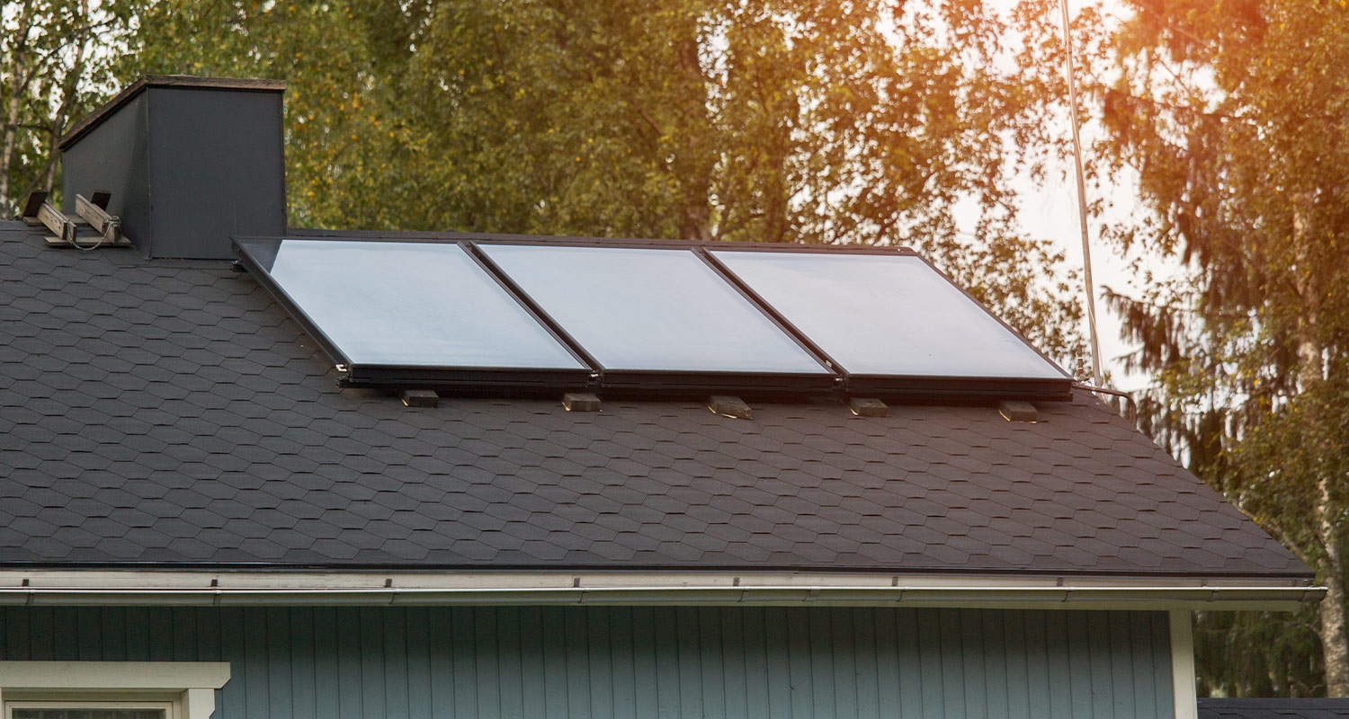 Turkoosin talon musta katto, jossa kolme aurinkopaneelia ja taustalla vihreitä puita