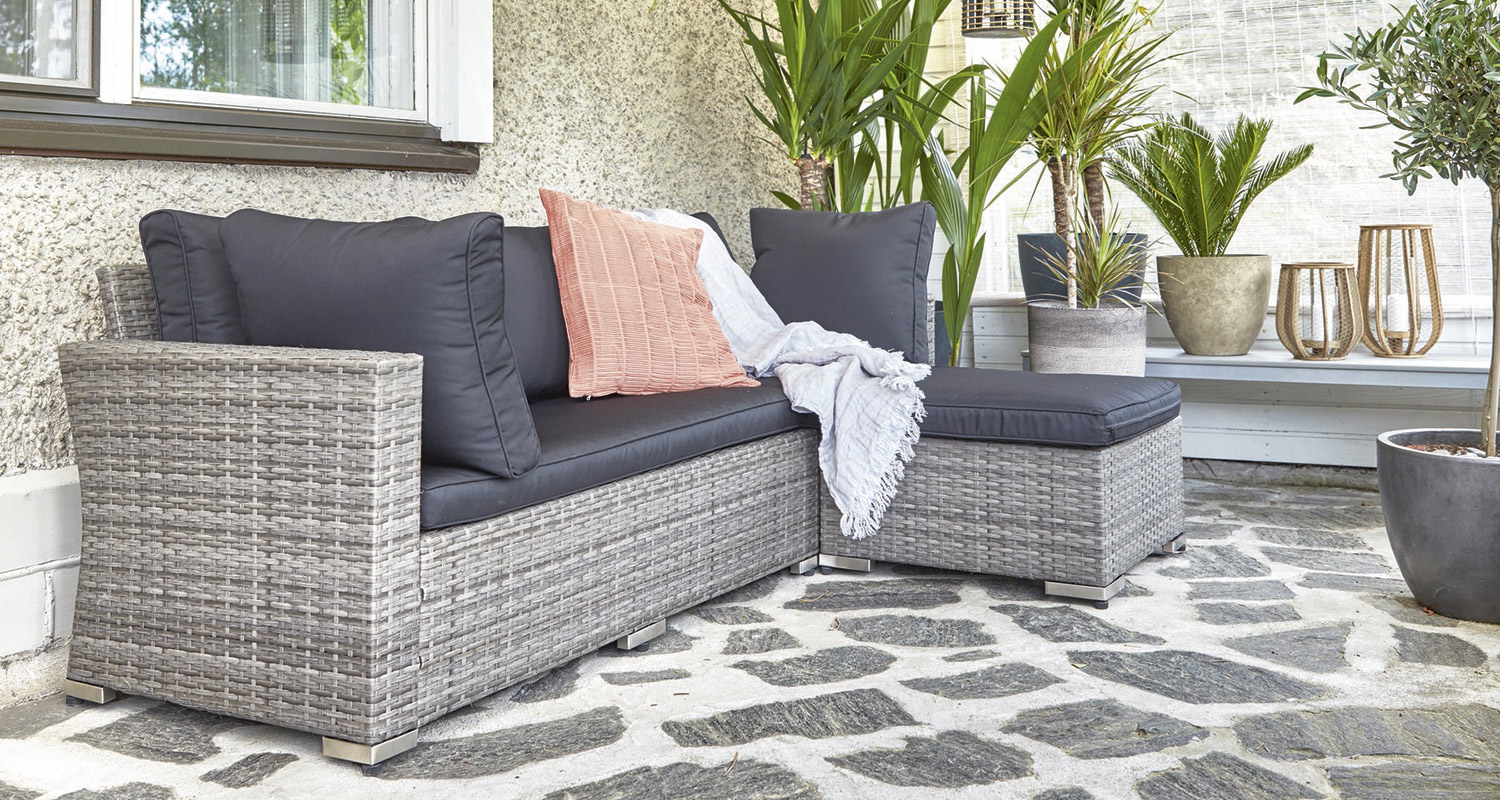 Harmaa korisohva tummilla tyynyillä, vaaleanpunainen tyyny, viltti ja viherkasveja