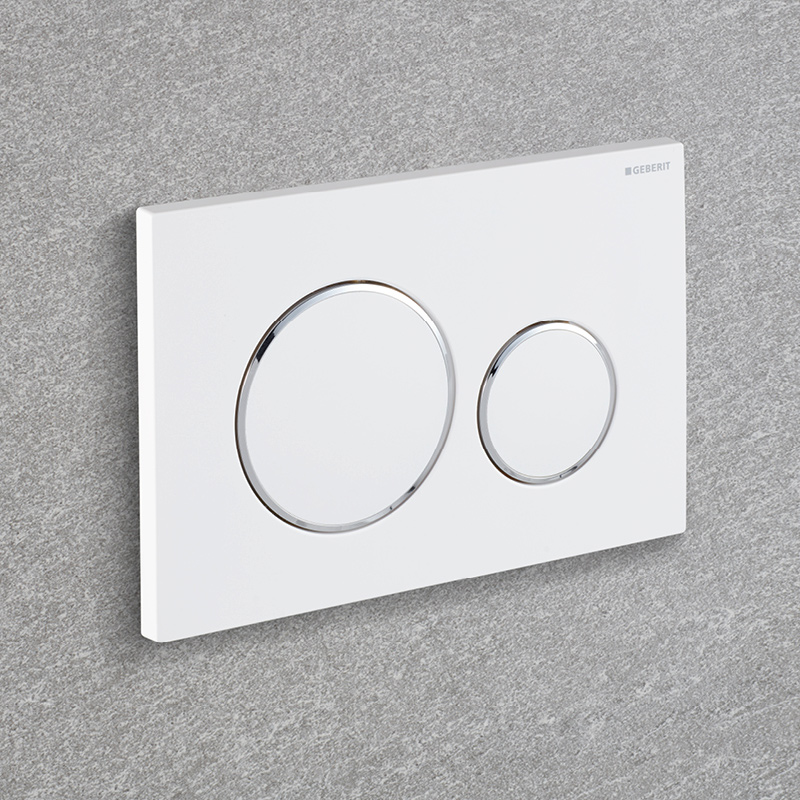 Valkoinen Geberit WC-painikelevy harmaalla kiviseinällä, iso ja pieni kromireunainen painike