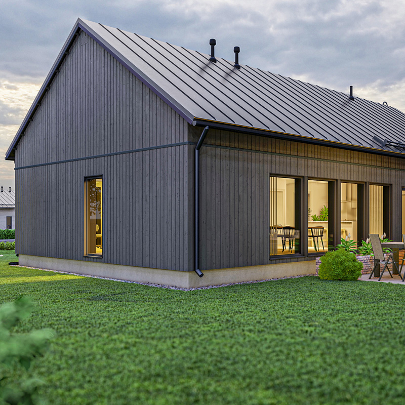 Moderni tumma puutalo harmaalla peltikatolla, keltainen sisävalo, vihreä nurmikko ja patioryhmä