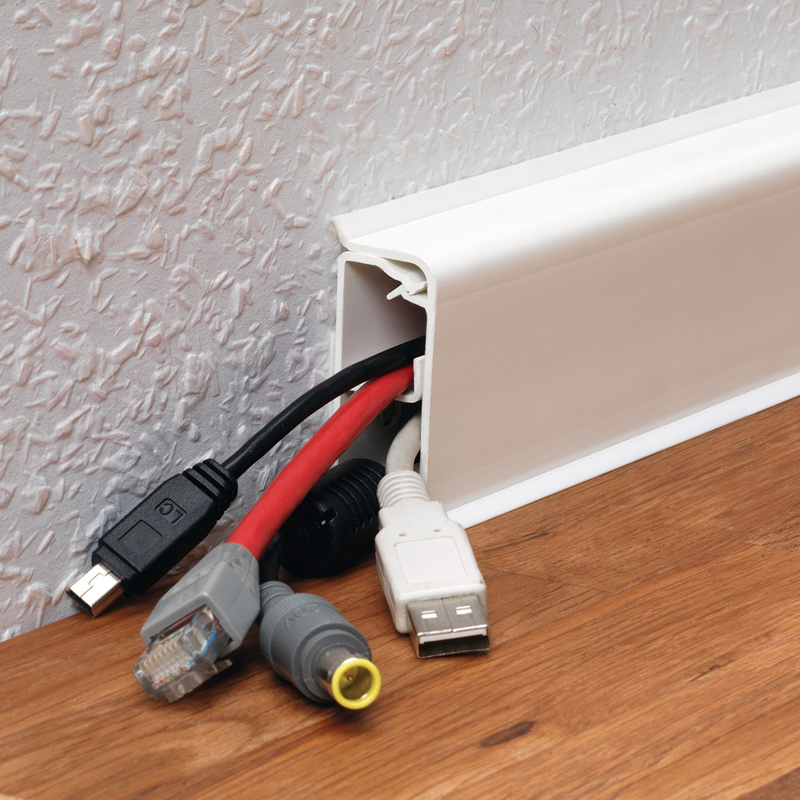 Valkoinen kaapelikanava puulattian reunassa valkoista seinää vasten, USB-, HDMI- ja verkkokaapeleita