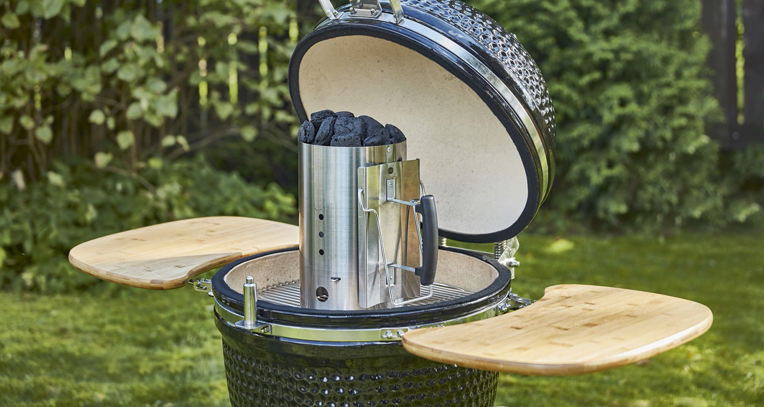 Avoin tummanvihreä kamadogrilli bambupöydillä ja teräspiipulla puutarhassa