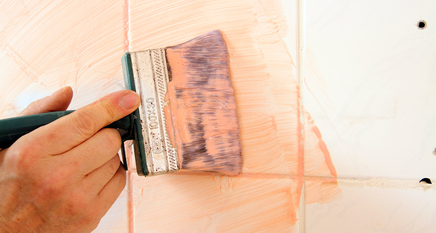 Käsi maalaa valkoisia laattoja vaaleanpunaisella siveltimellä.