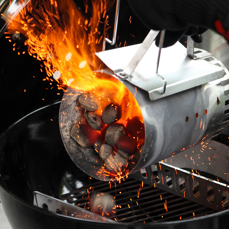 Henkilö kaataa kuumia, kipinöiviä grillihiiliä kiertoilmagrilliin