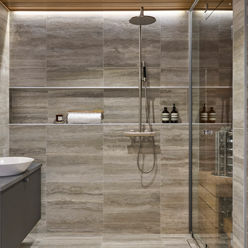 Greigen sävyinen kylpyhuone talotehtaan Showroomilla Vantaalla. Kuvan laatta Travertino 60x60 Silver R10/B. Laatat K-Raudan valikoimista.