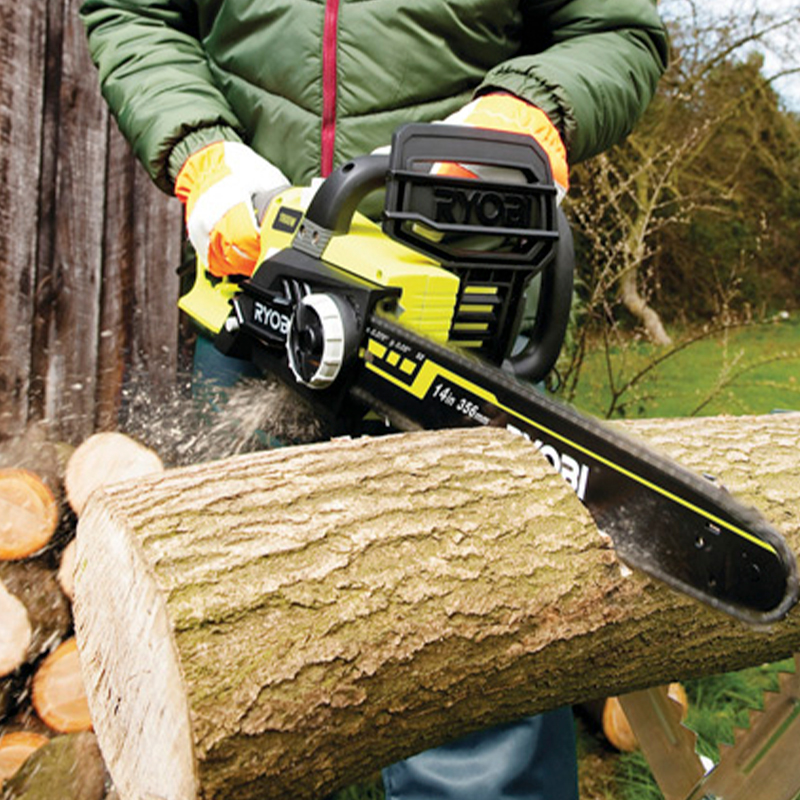 Henkilö vihreässä takissa ja oransseissa hansikkaissa sahaa halkoa vihreällä Ryobi-moottorisahalla.