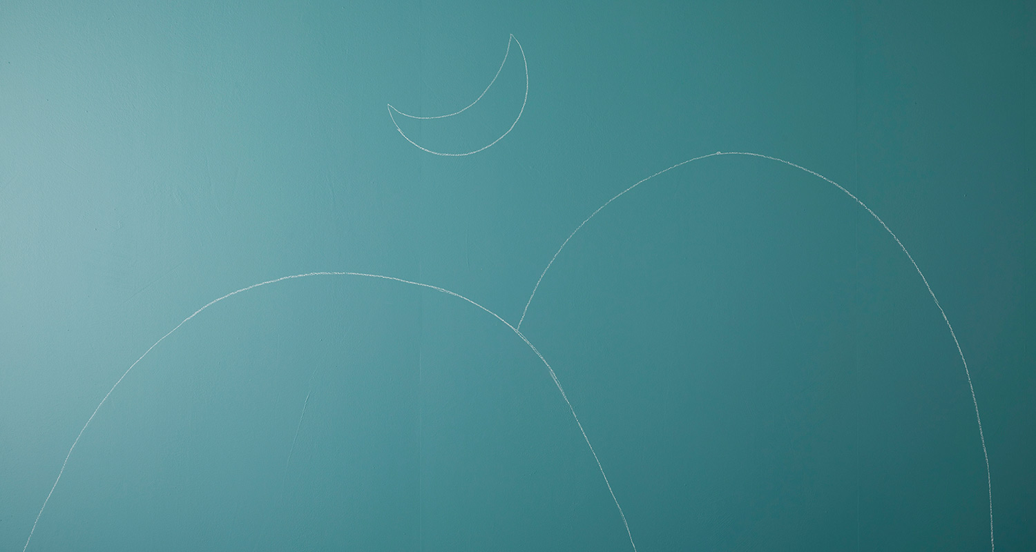 Vaaleanturkoosi seinä, jossa valkoisella liidulla piirretyt kukkulat ja sirppikuu.