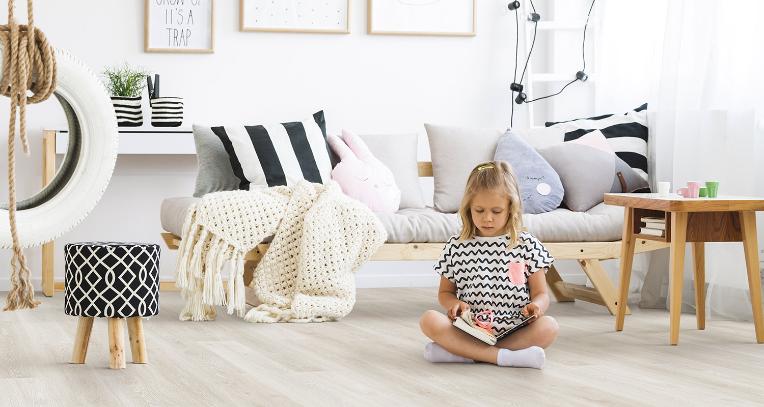 Lapsi lukee kirjaa vaalean muovimaton päällä istuen hauskassa huoneessa. 