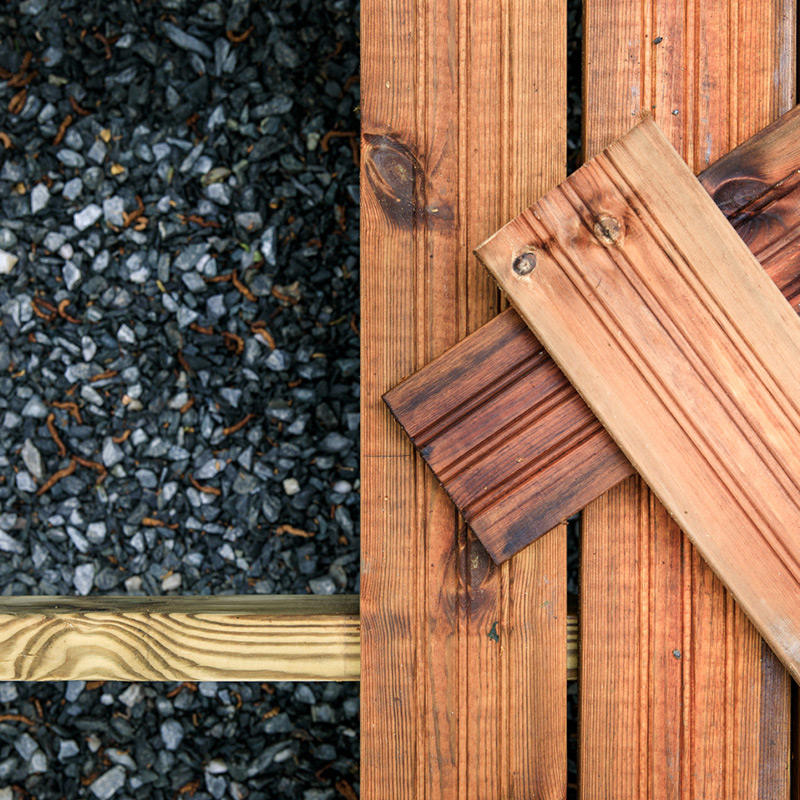 Tummanharmaata soraa ja rusehtavia puulautoja vierekkäin ja poikittain päällekkäin.