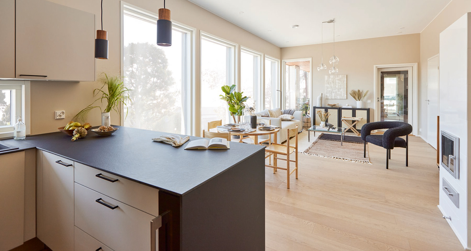 Valoisa avoin keittiö-olohuone mustalla saarekkeella, puulattia ja suuret ikkunat