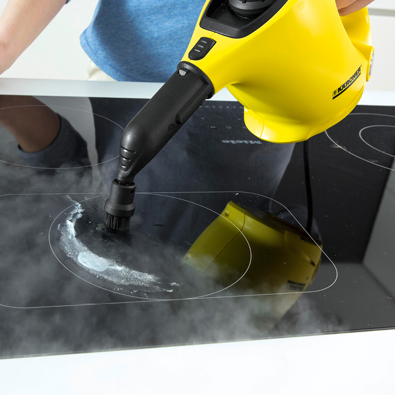 Keltainen höyrypuhdistin puhdistaa mustaa lasikeittotason pintaa harjalla ja höyryllä