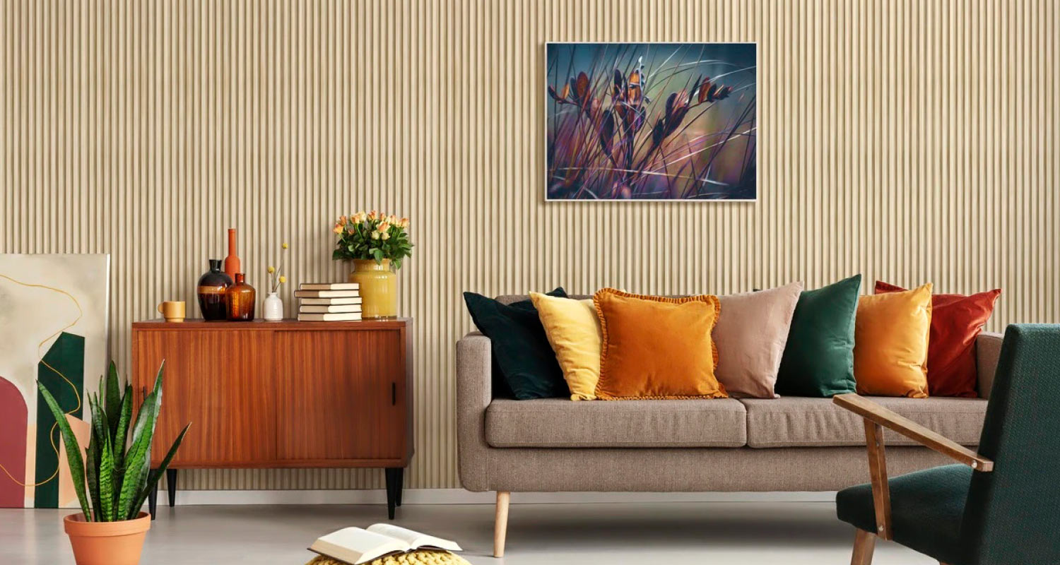 Olohuone beigen puupaneeliseinän edessä: harmaa sohva ja värikkäät tyynyt, lipasto, kukkia ja kasvi