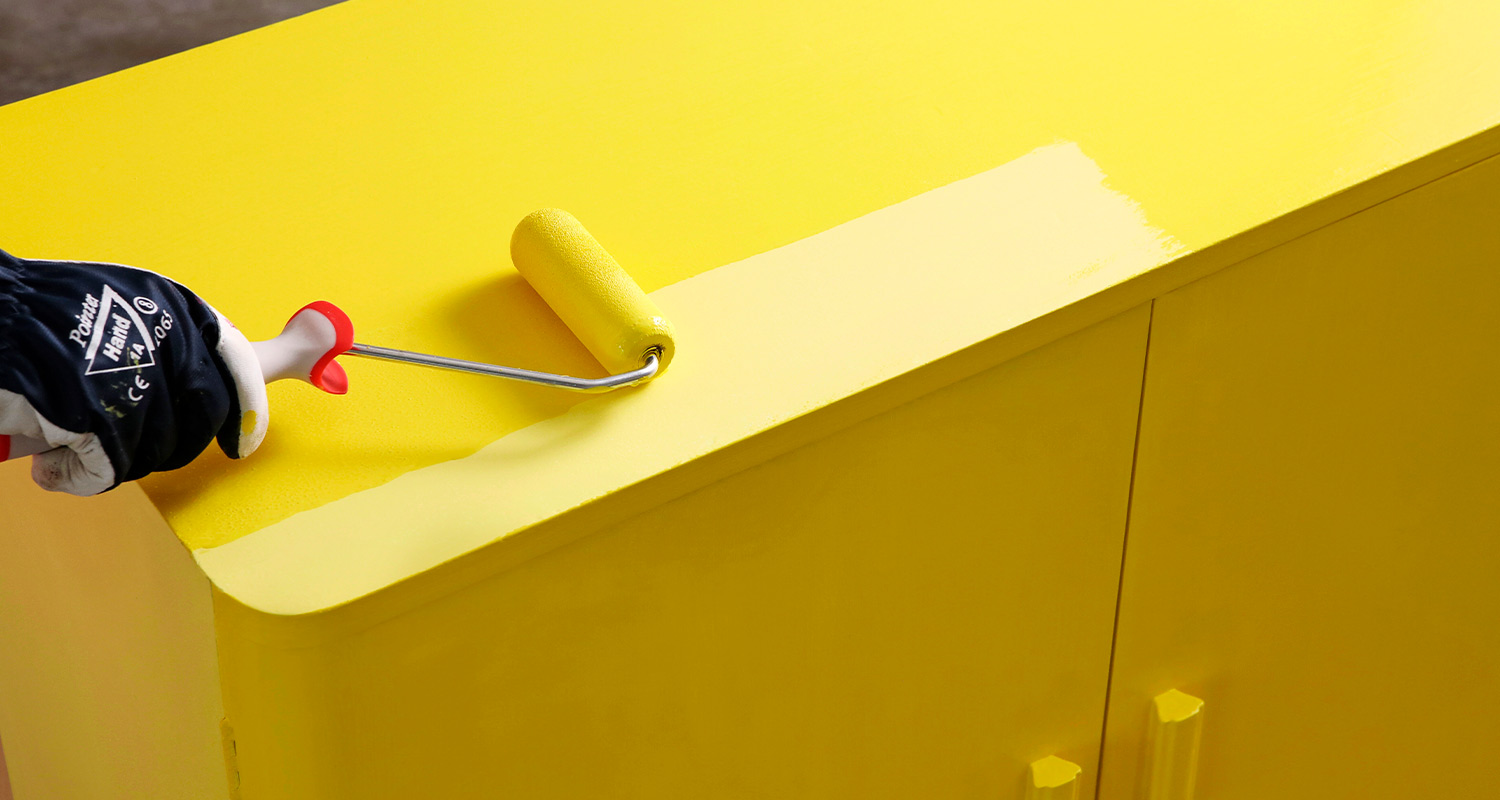 Tela levittää keltaista maalia lipastoon.