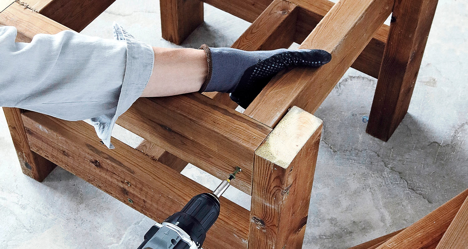 Mies rakentaa sadevesitynnyrin näkösuojaa. Kuvassa ruuvataan sadevesitynnyrin alustaa yhteen.