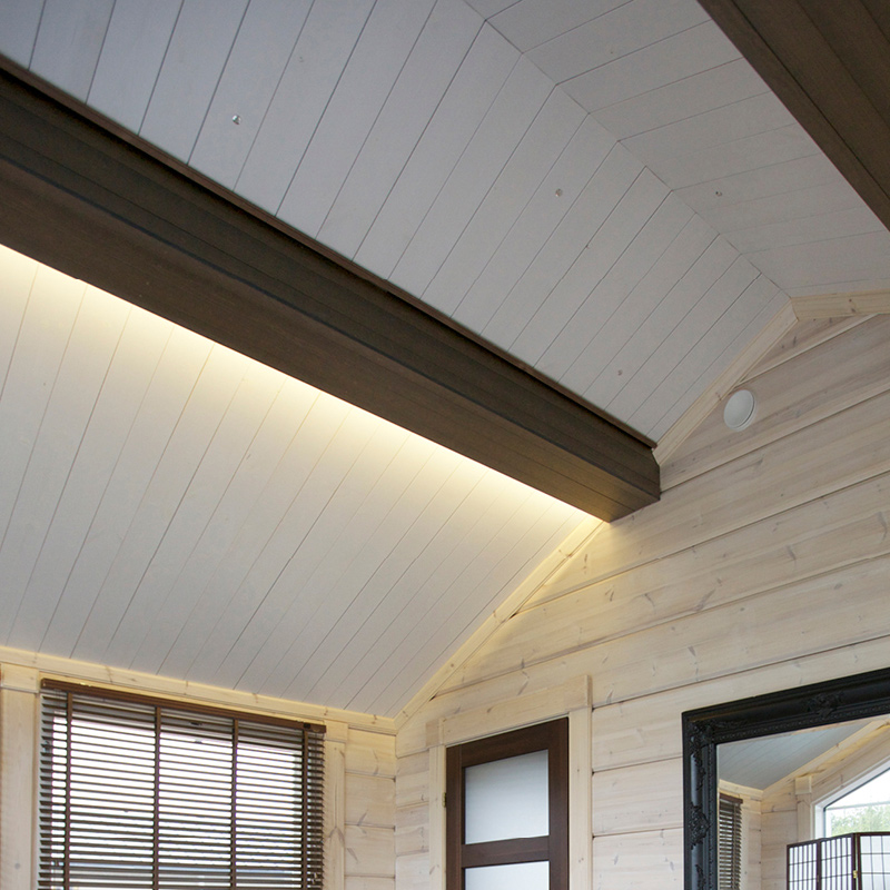 Moderni vaalea puinen huone, vino valkoinen paneelikatto, tumma palkki ja lämmin epäsuora valaistus.