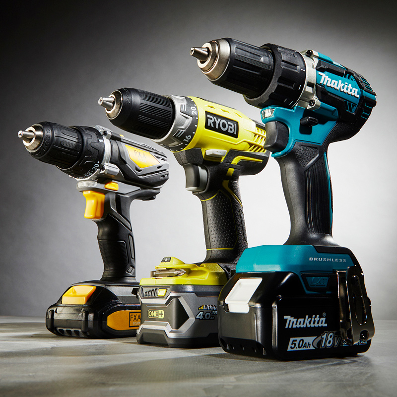 Kolme akkuporakonetta harmaata taustaa vasten: sininen, keltainen ja harmaa.