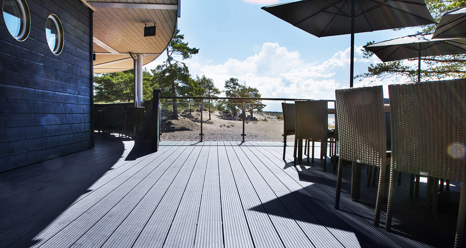 Rantaterassi harmaanlaudoituksella, korituoleilla, aurinkovarjoilla, mäntyhiekkadyynimaisemalla