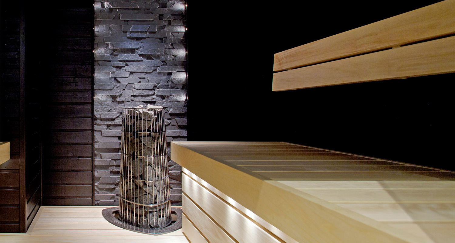 Moderni sauna: vaaleat lauteet, tummat kiviseinät ja kiuas kiuaskivillä.