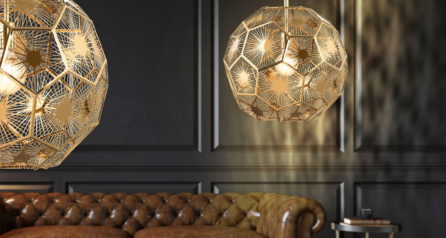 Kaksi kultapintaista geometristä valaisinta harmaata paneeliseinää vasten, alla ruskea nahkasohva.