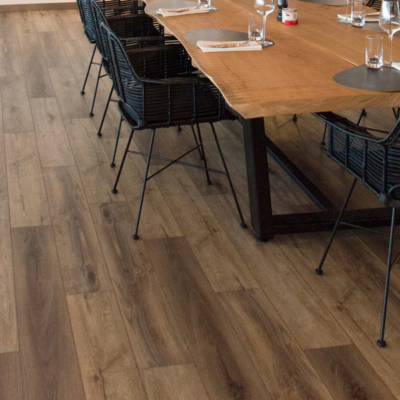 Pitkä vaalea puupöytä mustilla rattan-tuoleilla sisätilassa, lasit ja lautasliinat.