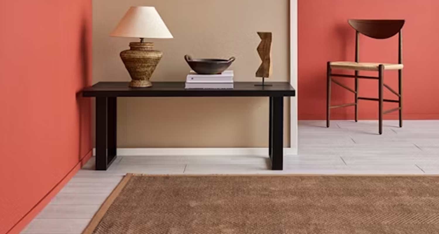 Mustan penkin edessä punertava ja beige seinä, penkillä lamppu, kulho ja veistos, vieressä puutuoli.