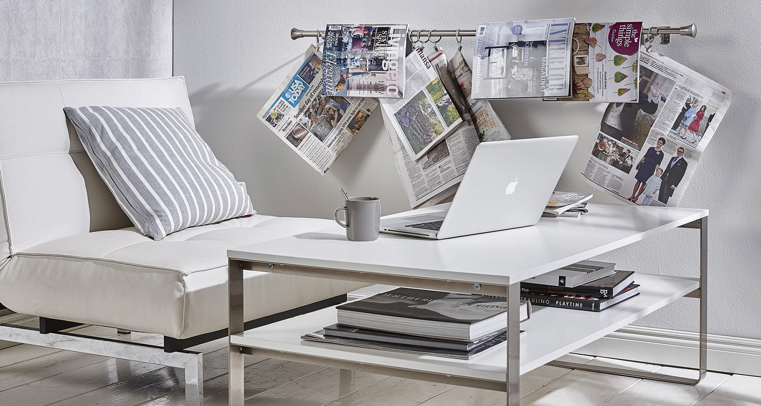 Valkoinen sohva raidallisella tyynyllä, pöydällä MacBook ja muki, seinällä ripustetut lehdet