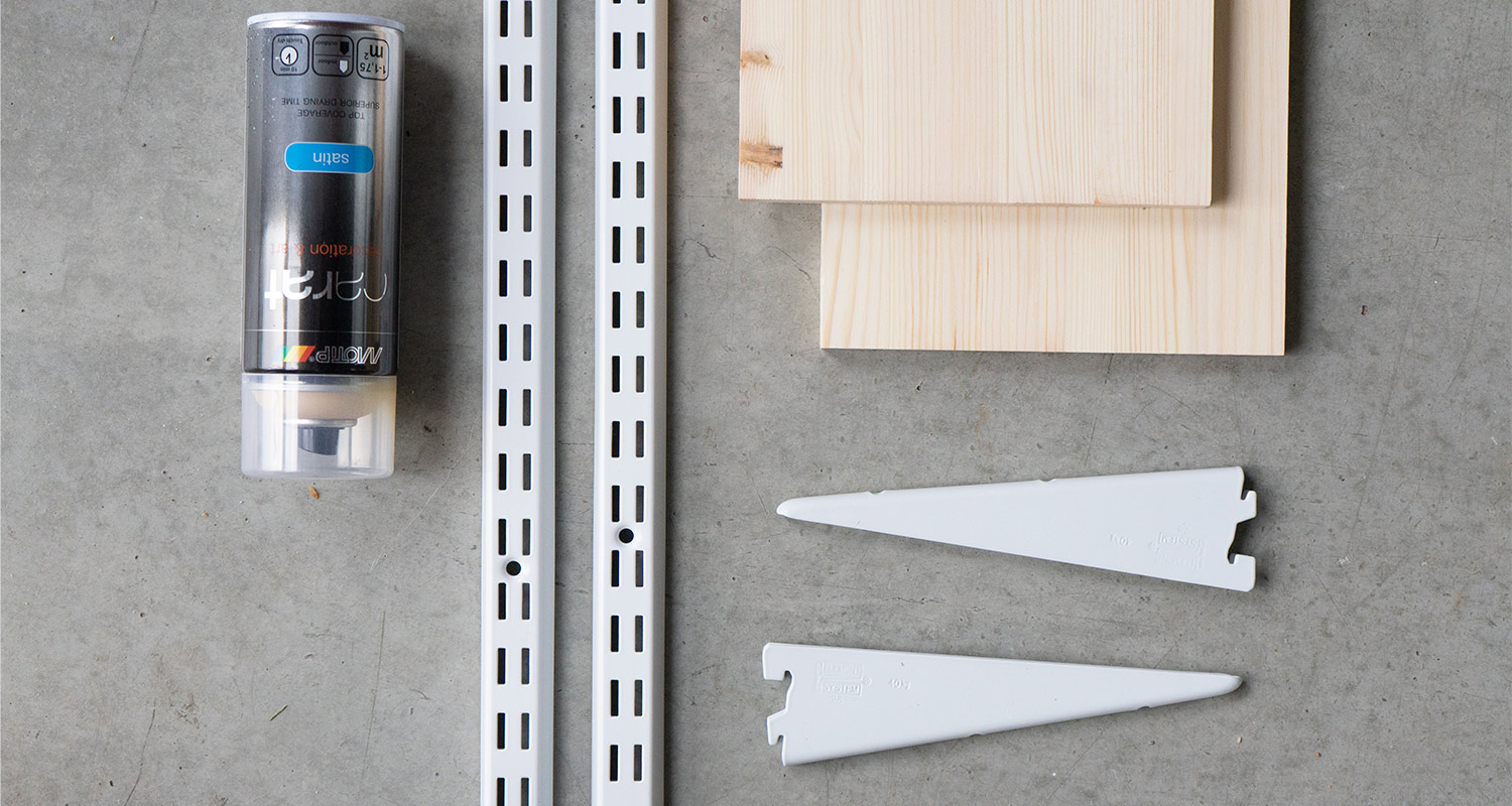 Betonitaustalla hopeinen puukittitubi, valkoiset kiskot ja kannattimet sekä vaaleat puulaudat