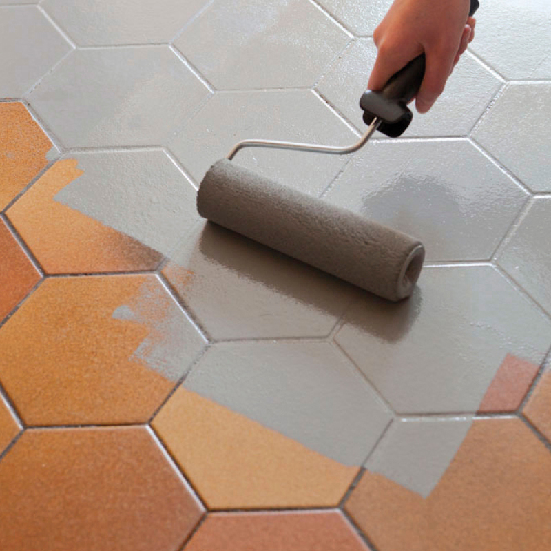 Kuvassa laattalattiaa maalataan harmaalla kaakelimaalilla. Maalia on telassa ja sitä levitetään lattialle.