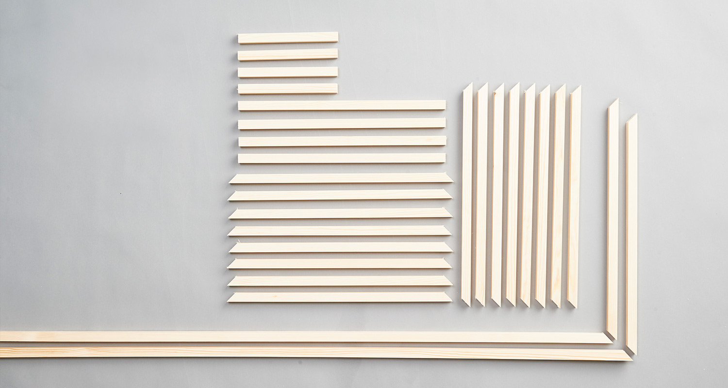 Vaaleat puulistat pituuden mukaan riveihin järjestettyinä harmaalla alustalla.