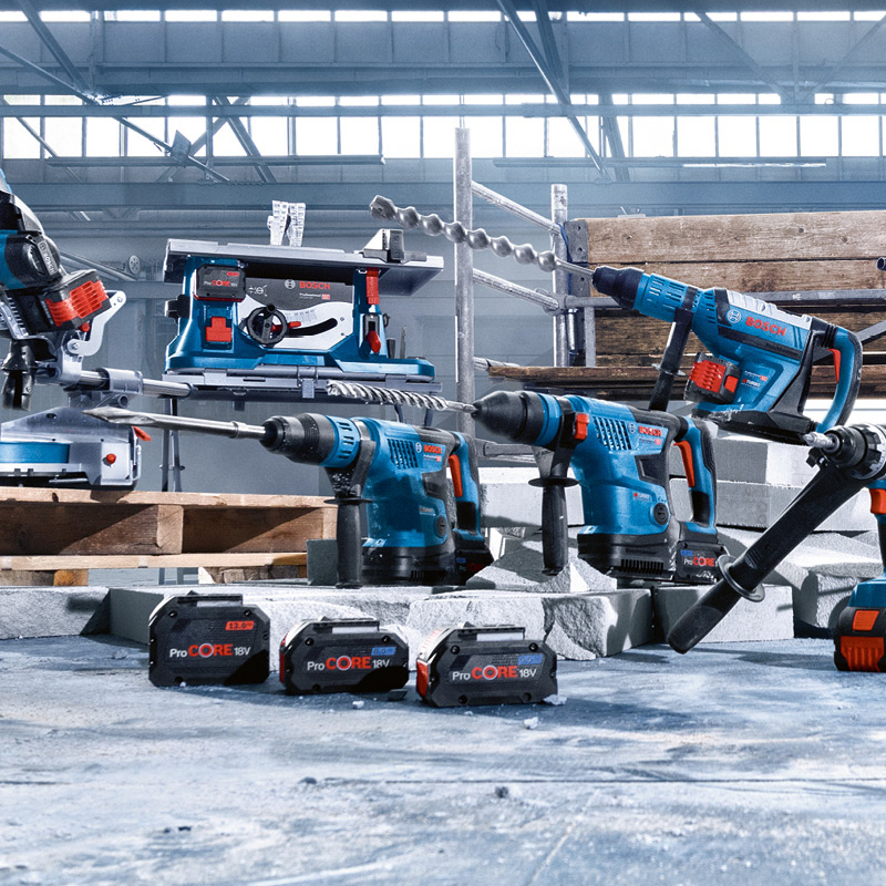 Siniset ja punaiset akulliset työkalut (porat, vasara, sirkkeli) ja ProCORE 18V-akut tehdashallissa
