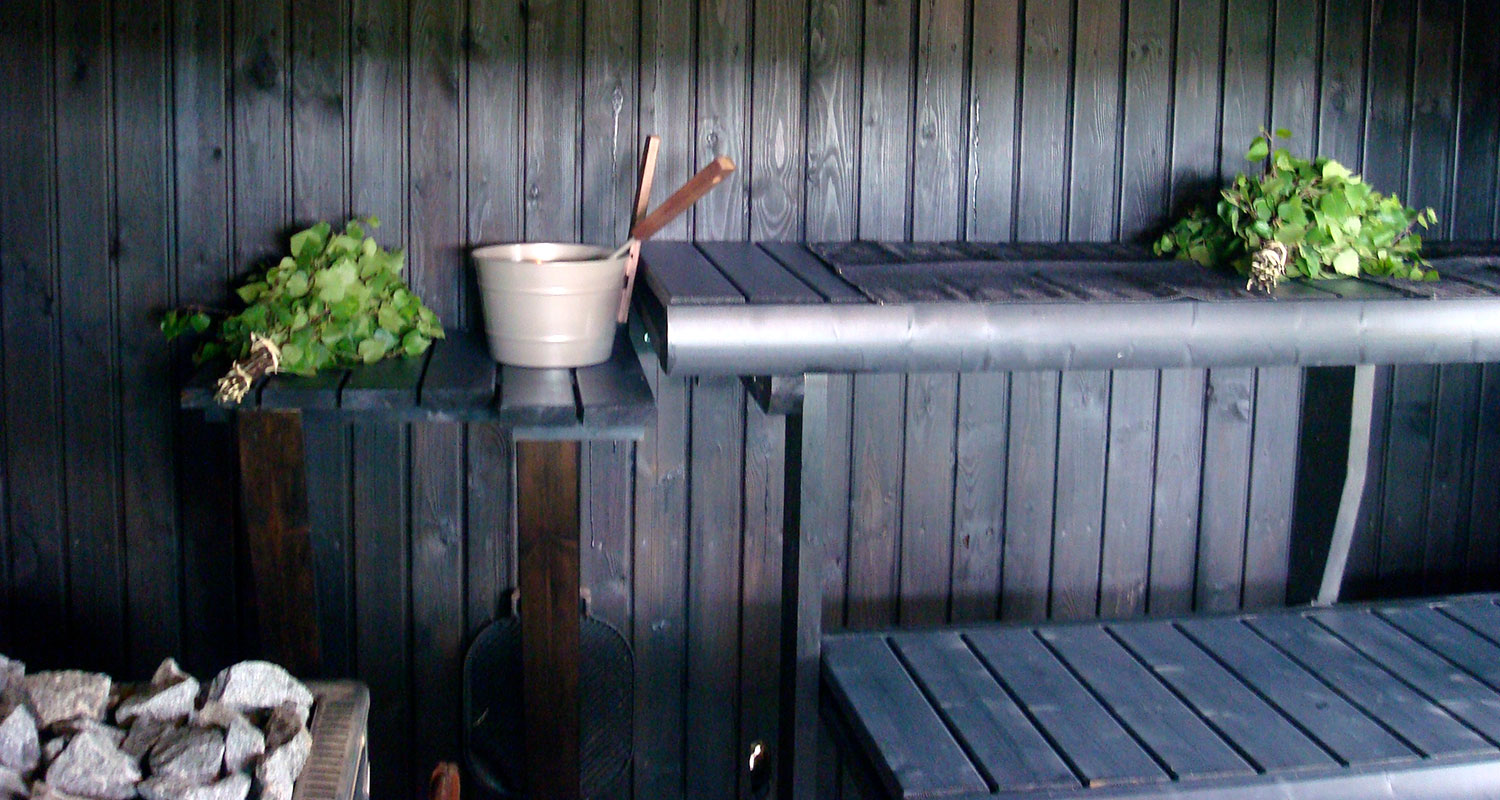 Saunassa mustat puupaneelit ja lauteet, vihdat sekä beige kiulu kauhalla.