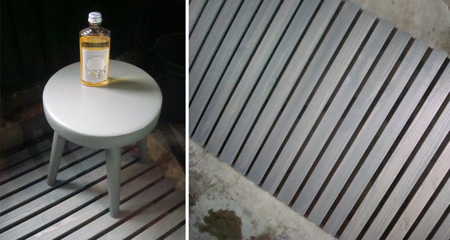 Vaaleanharmaa kolmijalkainen jakkara harmaalla puulattialla päällä pieni keltainen pullo