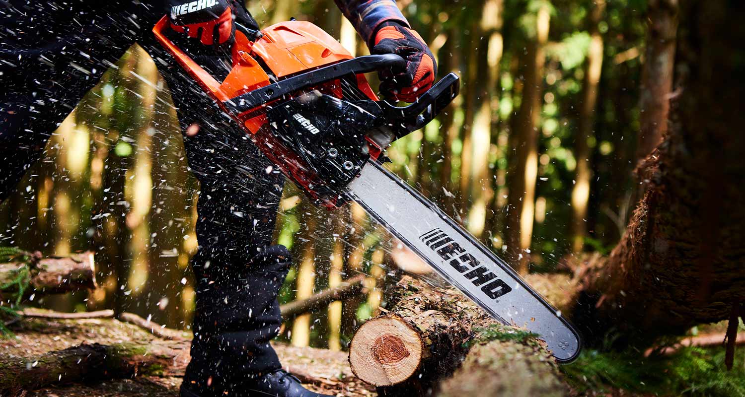 Oranssi ECHO-moottorisaha sahaamassa puunrunkopalaa metsässä, puunsirut lentävät