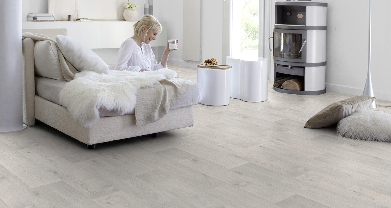 Vaalea muovimatto vaaleassa modernissa olohuoneessa, jossa nainen juo maitoa isolla sohvalla