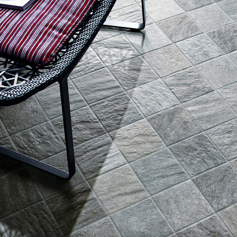 Mustametallinen tuoli, punavalkoraidallinen tyyny ja harmaa neliölaattalattia