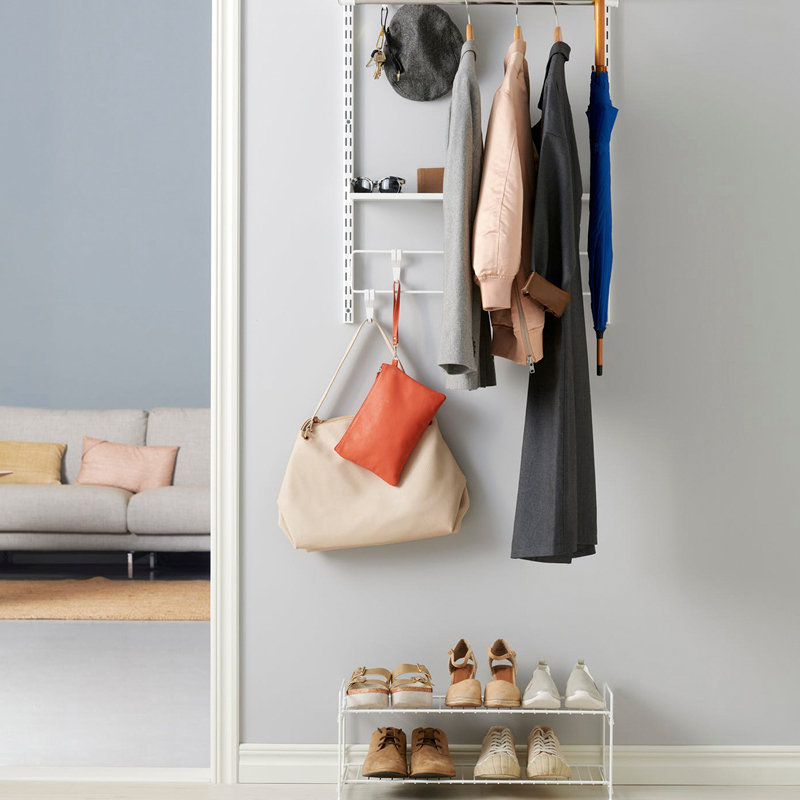 Vaalealla seinällä valkoinen naulakko takit, hattu, sininen sateenvarjo, laukut ja kenkäteline.