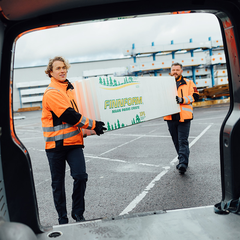 Työmiehet kantavat eristelevypakkausta pakettiautoon.