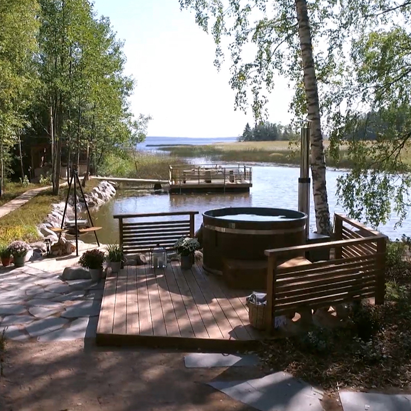 Puinen terassi ja kylpytynnyri järven rannalla koivujen varjossa.