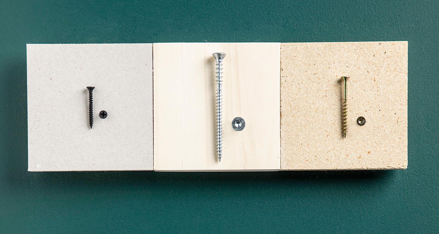 Kolme vaakalevyä (harmaa, vaalea, lastulevy) tummanvihreällä taustalla, jokaisessa ruuvi ja kanta.