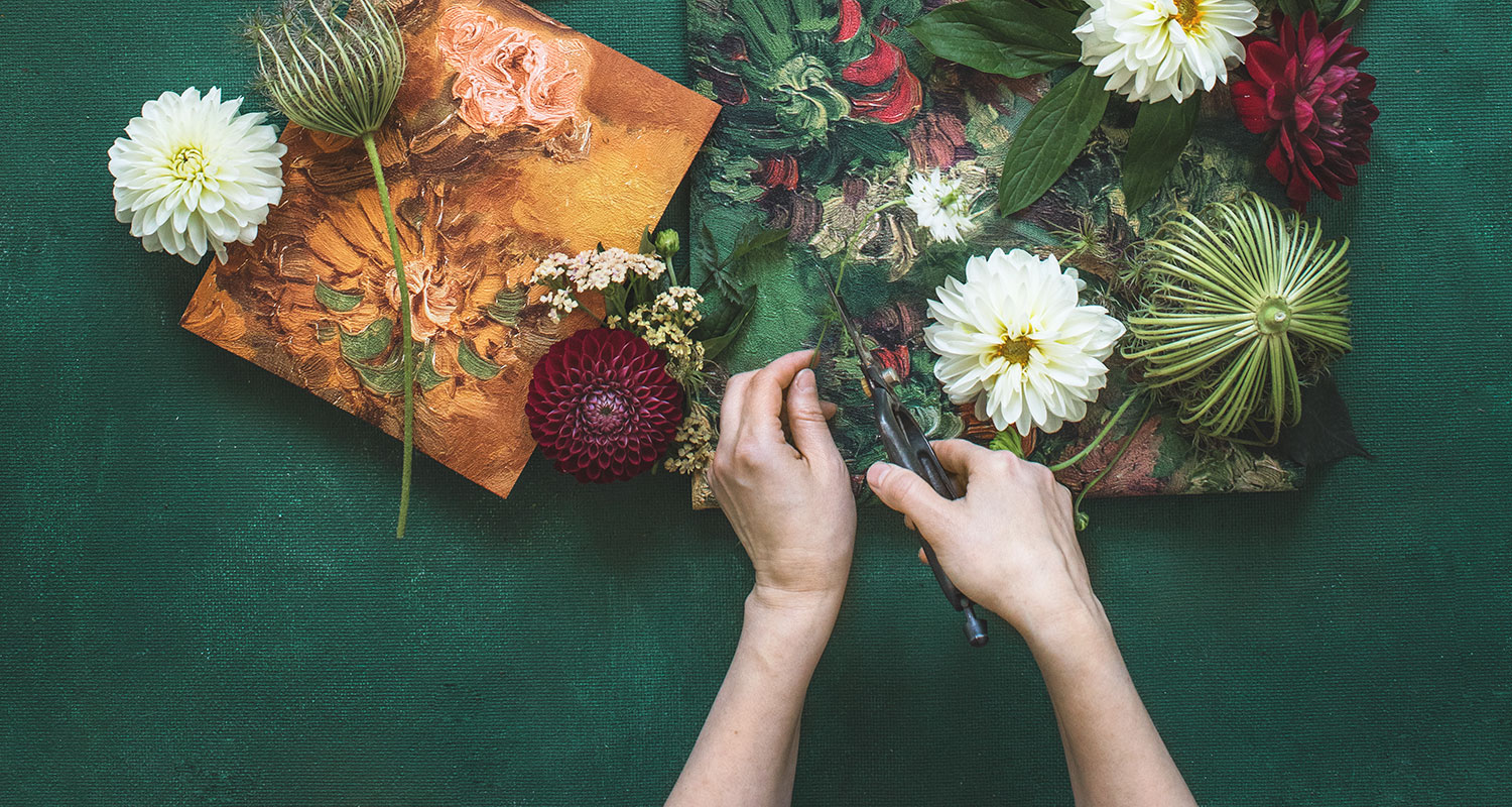 Vihreällä taustalla leikataan valkoista kukkaa kullankeltaisten ja vihreiden kukkamaalausten vieressä