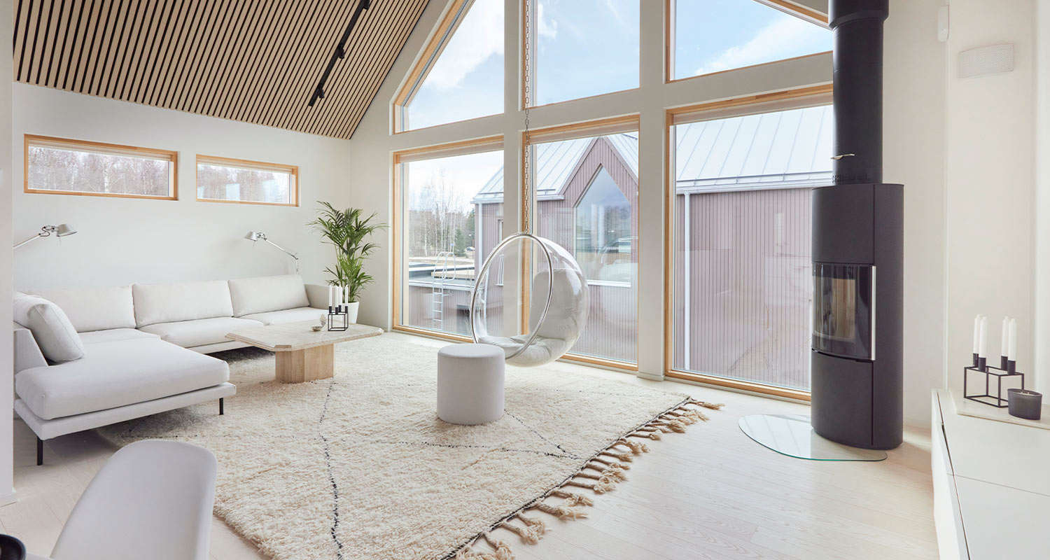 Vaalea olohuone isolla ikkunalla, valkoinen kulmasohva, roikkuva läpinäkyvä tuoli ja musta takka