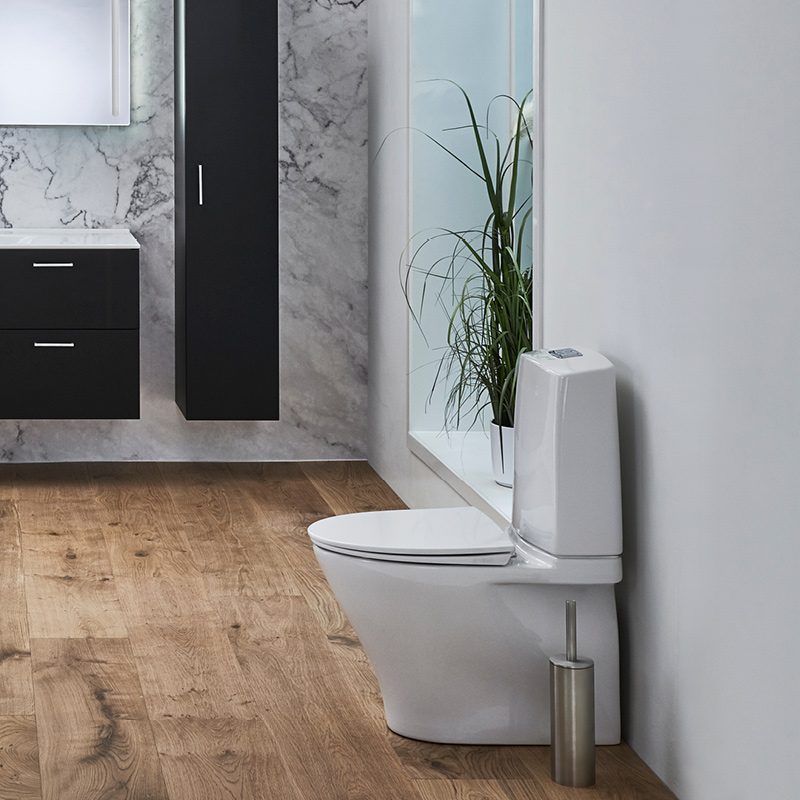 Moderni kylpyhuone: valkoinen WC-istuin puulattialla, marmoriseinä ja mustat kaapit viherkasvilla.